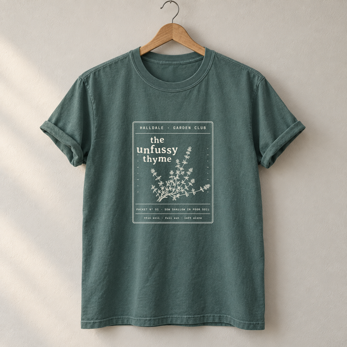 The Unfussy Thyme tee in Blue Spruce, on a hanger