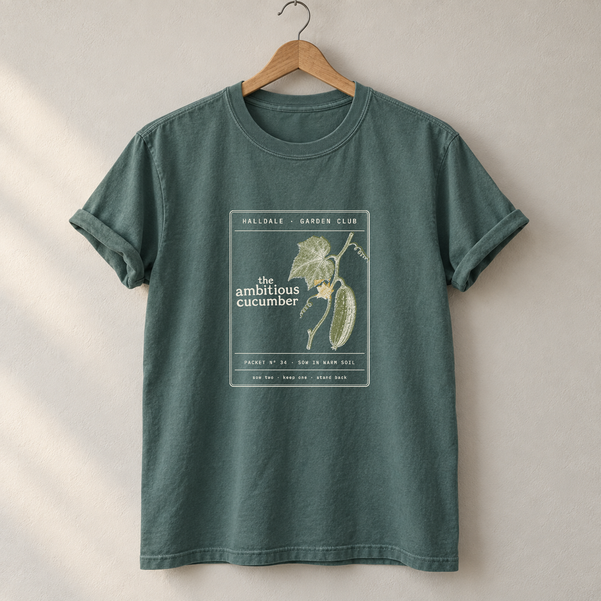The Ambitious Cucumber tee in Blue Spruce, on a hanger