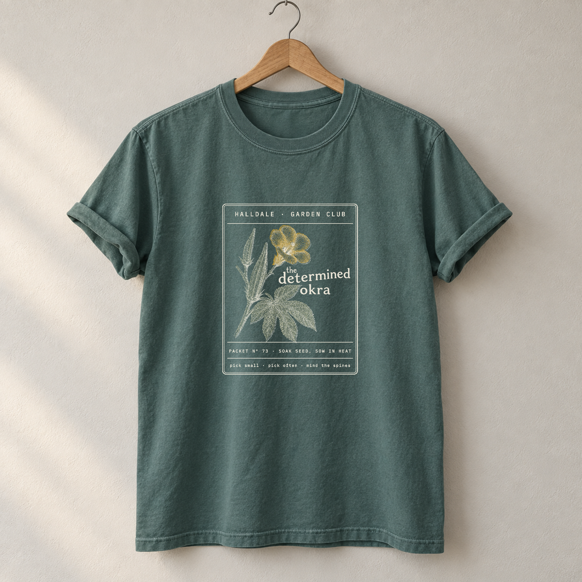 The Determined Okra tee in Blue Spruce, on a hanger