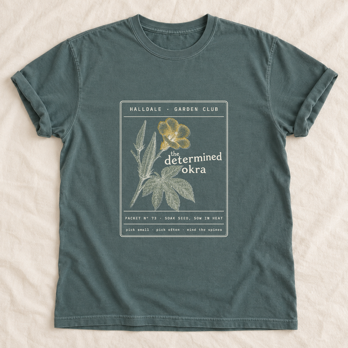 The Determined Okra tee in Blue Spruce, laid flat