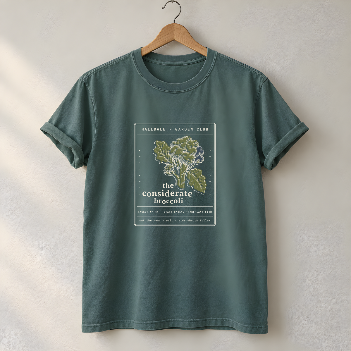 The Considerate Broccoli tee in Blue Spruce, on a hanger