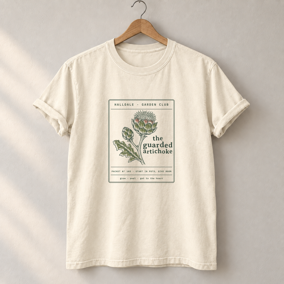 The Guarded Artichoke tee in Ivory, on a hanger