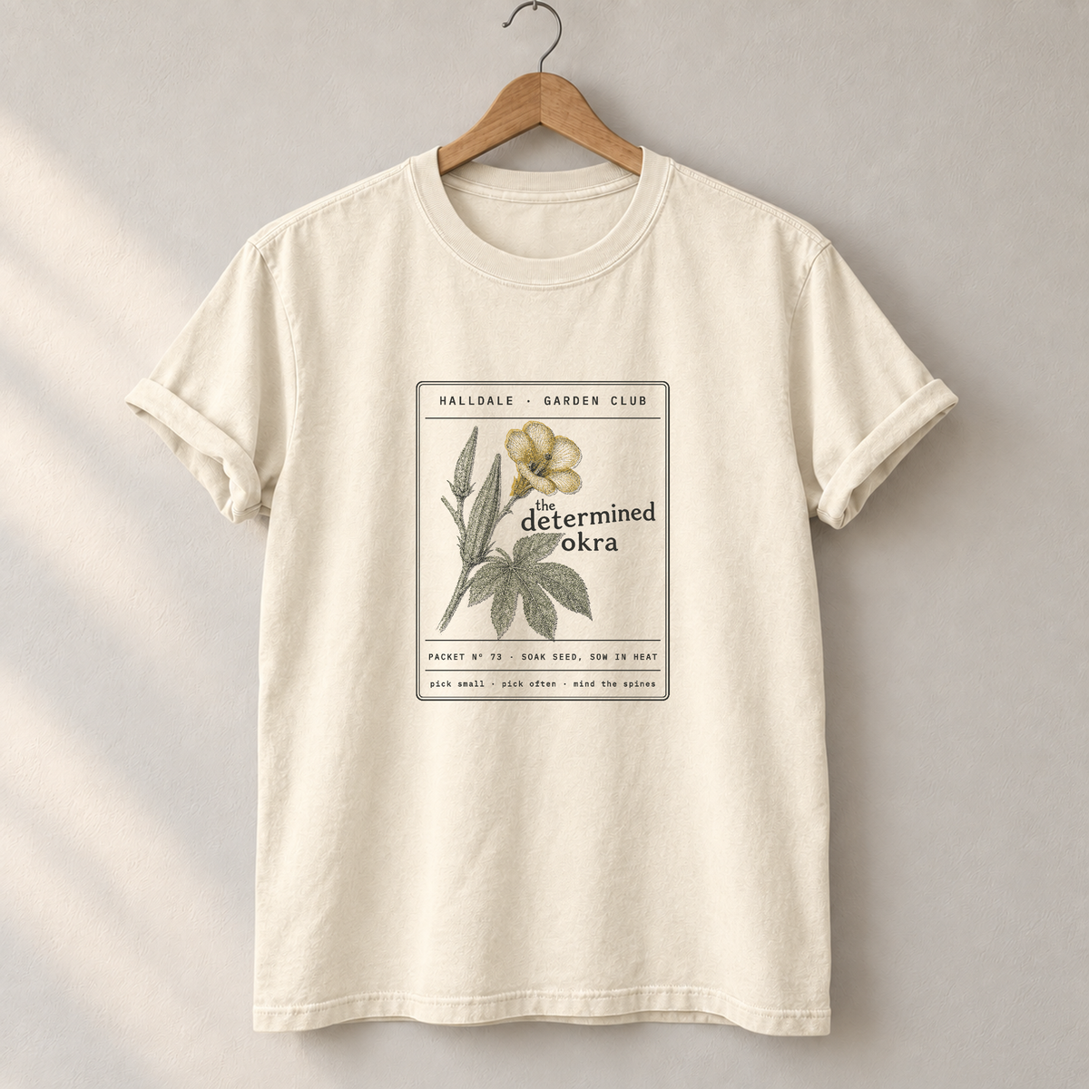 The Determined Okra tee in Ivory, on a hanger