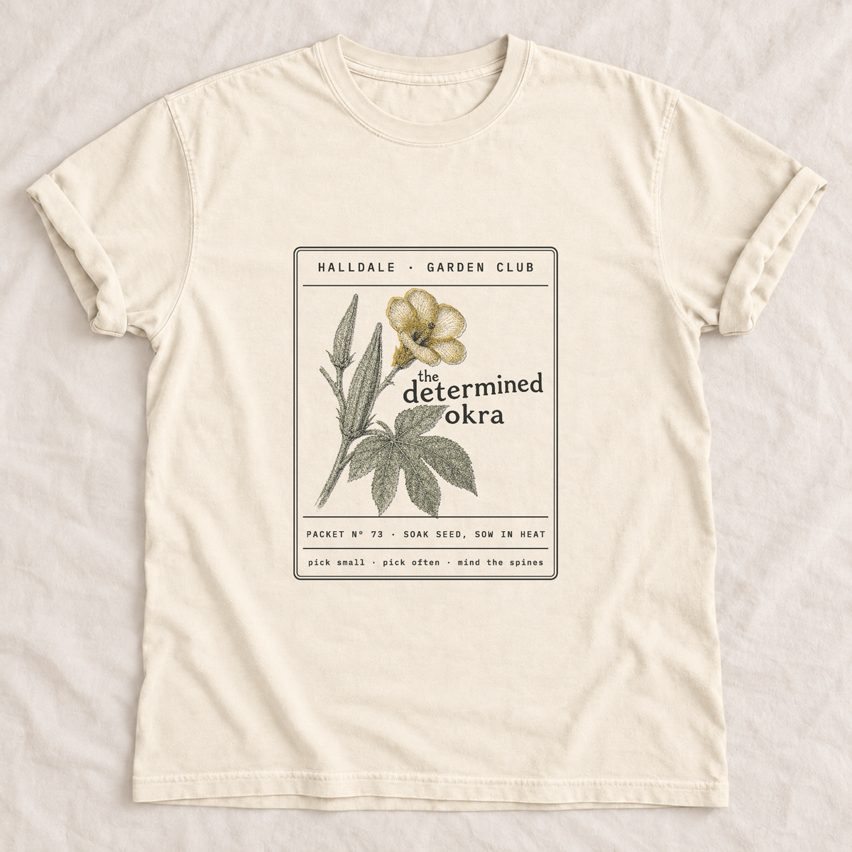 The Determined Okra tee in Ivory, laid flat