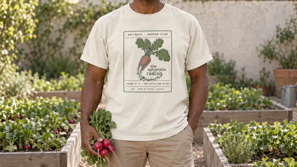A man in the Ivory Optimistic Radish tee stands by raised vegetable beds with neat rows of radish leaves, holding a bunch of fresh red radishes with their leafy tops.