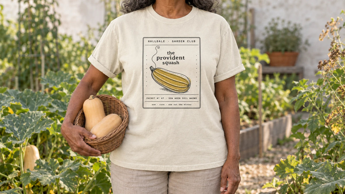 A woman in the Ivory Provident Squash tee stands by sprawling winter squash vines in early fall, holding a shallow wicker basket holding two butternut squash.