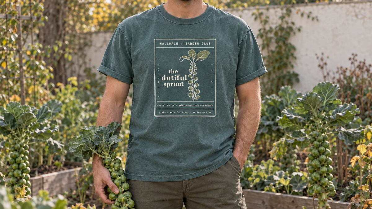 A man wearing the updated Dutiful Sprout tee in Blue Spruce, holding a Brussels sprout stalk in a late fall brassica garden.