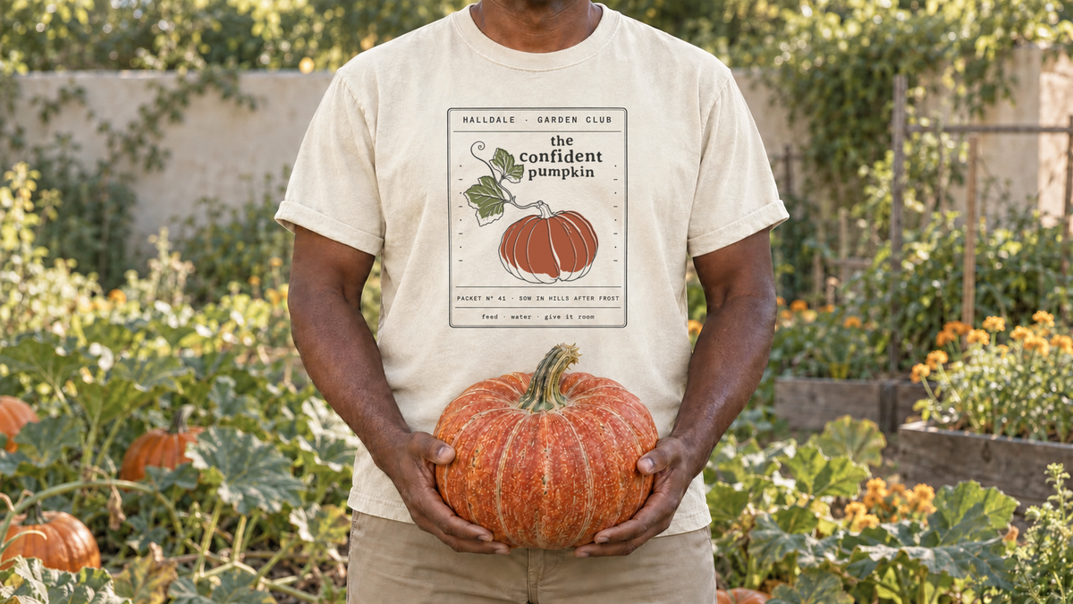 A man wearing the revised two-leaf Confident Pumpkin tee, holding a pumpkin in a sunny garden.